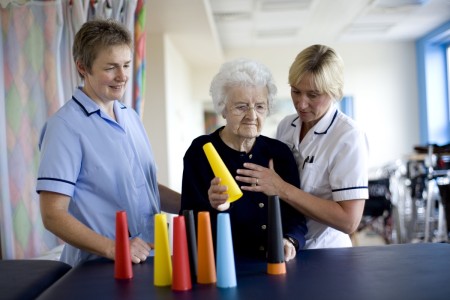 Two physiotherapists with an elderly woman doing a hand exercise with multi-coloured plastic cones