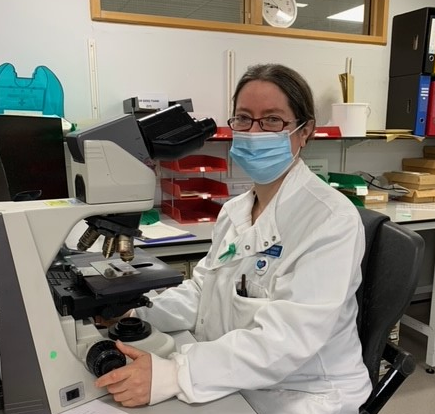 A woman sat by a microscope wearing a lab coat.