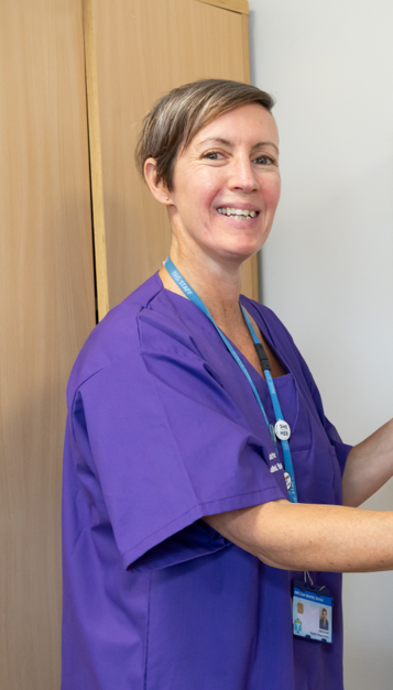 A lady wearing a purple scrub top with short hair smiling at the camera.