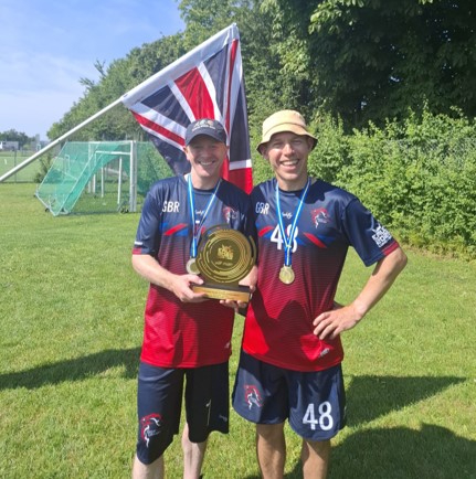 Two men standing together in GB sports tops holding a trophy and wearing a medal