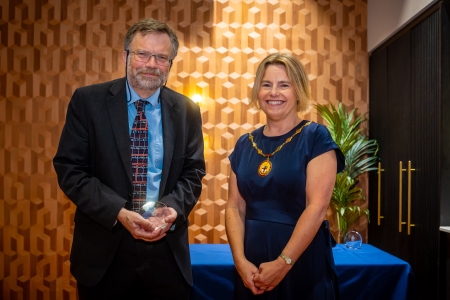 2 people stood together with one holding an award.