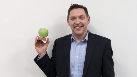 A photograph of a man holding an award. The awards looks like a green apple.