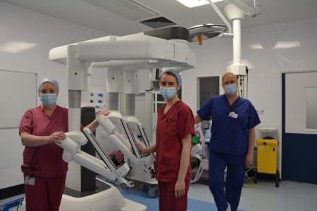 Three women in scrubs standing next to a piece of robotic equipment.