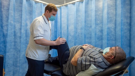 A patient lying on a bed with a physio stretching the patient's leg.