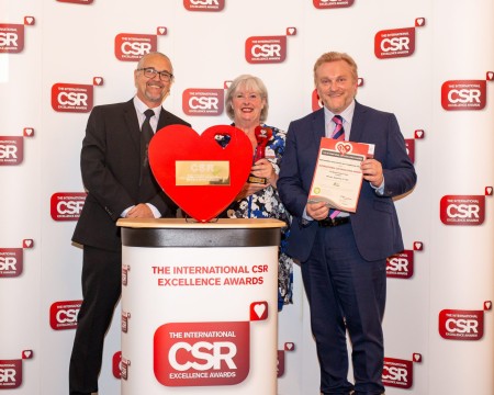 A photograph of two men and a woman. The women is holding a trophy and one of the men is holding a certificate.