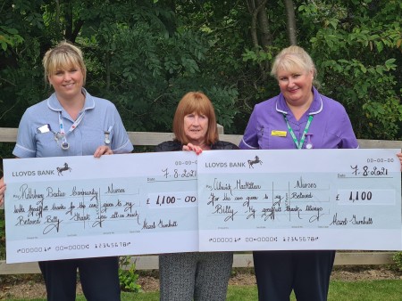 Three women holding two large cheques.