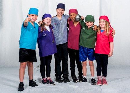 A group of children wearing mini scrubs with different NHS job roles.