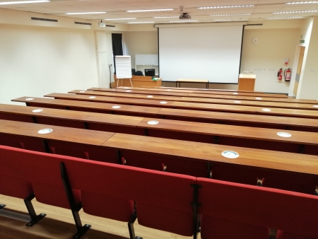 A picture of a lecture theatre with red long seats and oak wood long tables