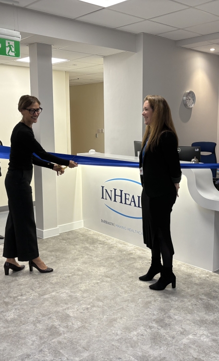 Two people stood by a blue ribbon with one about to cut it with scissors.