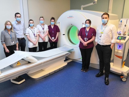 Seven members of staff standing next to a CT scanner