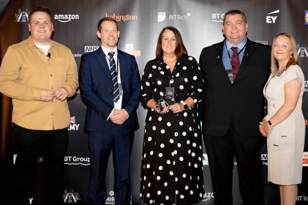 A group of five people. The woman in the middle is holding an award.