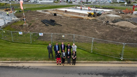A drone footage shot of a group of people smiling with a helipad construction in the background.