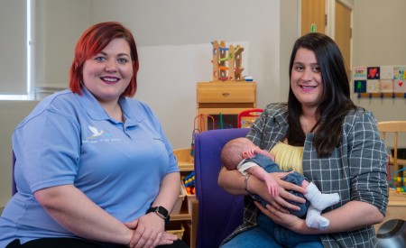 Two women siting. One of them is holding a baby.