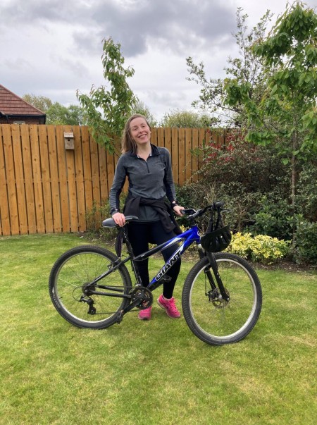 A woman with brown hair standing with a bike.