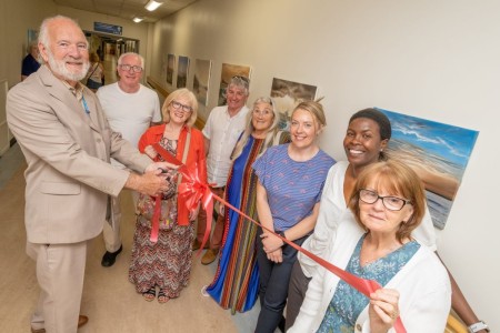 A group of people holding a long red ribbon and one of the men is cutting it.