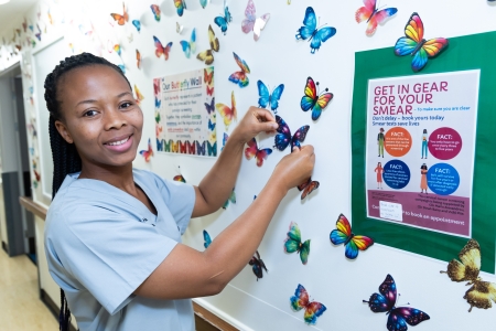 Girl wearing a light blue scrub top sticking a paper butterfly on a wall 