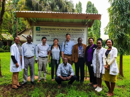 A group of people standing next to a sign for the 'Kilimanjaro School of Pharmacy'.