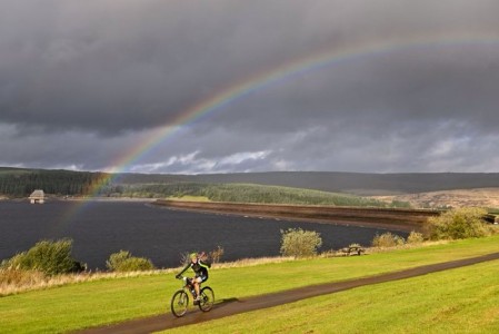 A cyclist with a rainbow behind them.