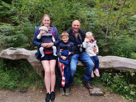 A family sat on a log. Two adults and three children.