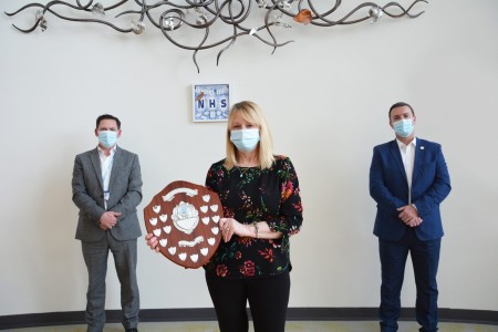 A photograph of three people, the woman in the middle is holding an award.