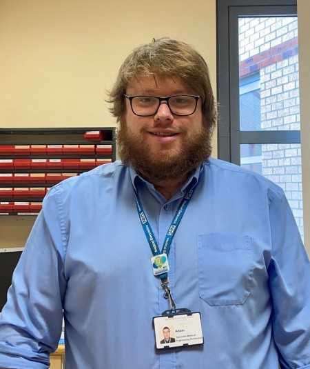 A man with brown hair and a beard, wearing a blue shirt.