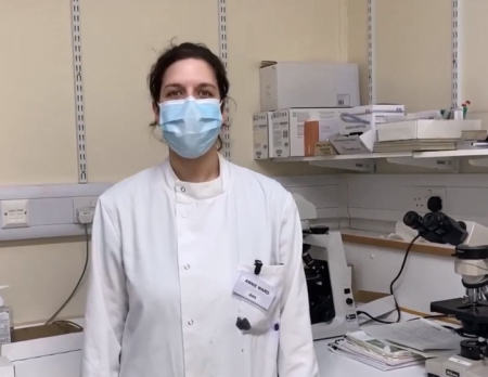 A woman with dark hair wearing a lab coat.