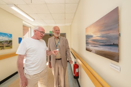 Two men looking at a piece of artwork on the wall.