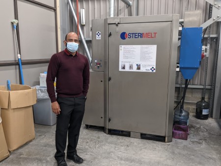 A photograph of a man stood next to a machine.