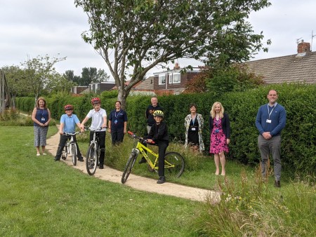 Six adults standing with three children on bikes in front of them