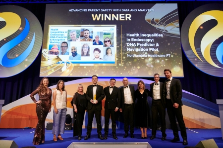 A line of people with a trophy on a stage in front of a screen with the award name.