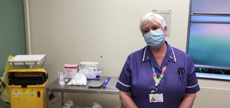 A photograph of a nurse standing next to a table that i set up for a vaccination.