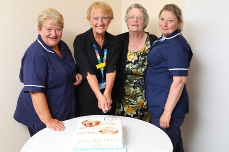 Four women. one of them is cutting a cake.