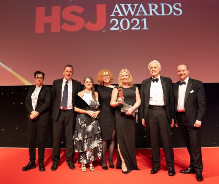 A group of men and women wearing a mix of suits and smart black dresses. One of the women is holding an award.