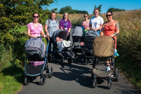 A photograph of six women standing outside. Five of them are pushing prams and one of the babies is visible.