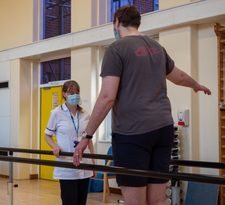 A man walking between two beams for assistance and a physio observing him.