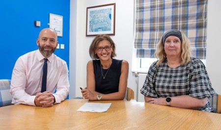 3 people sat a table. The woman in the middle has a piece of paper that she has signed on the table in front of her.