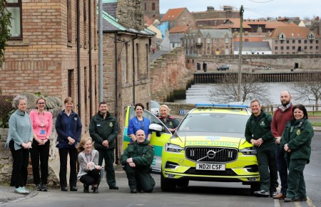 A group of paramedics with other staff members next to an ambulance car.