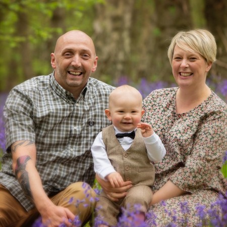 A photograph of a man and a woman holding a baby. They're all smiling.