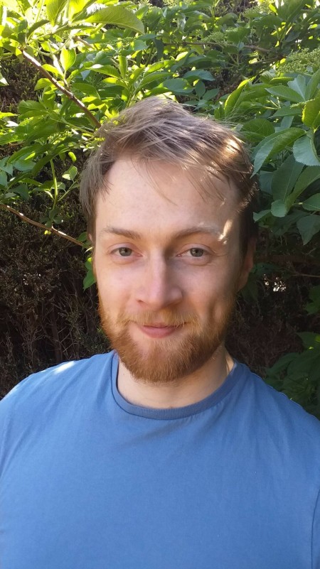 A portrait of a male standing in front of some leaves.