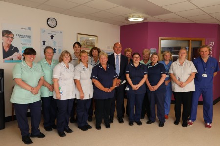 A group of healthcare staff and a man standing by a ward reception.