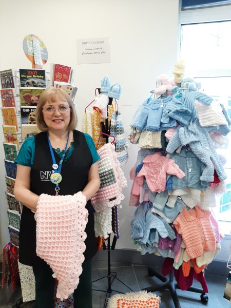 A woman stood next to a display full of knitted baby clothes.