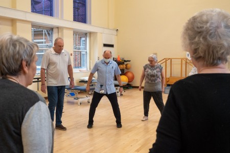 A group of people in a circle being led by a male physio.