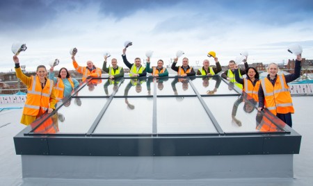 A group of people all wearing hi-vis vests and holding their helmets up in the air.