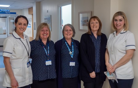 Five female staff members standing next to each other smiling and looking towards the camera.