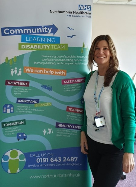 A woman standing next to the Community learning disability team banner.