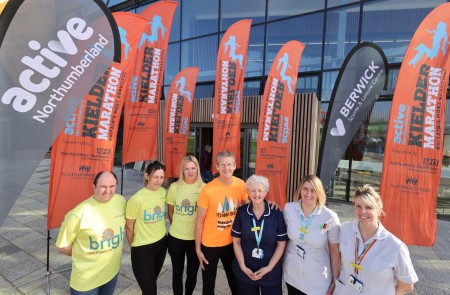 A photograph with seven people with active Northumberland and Kielder marathon flags in the background