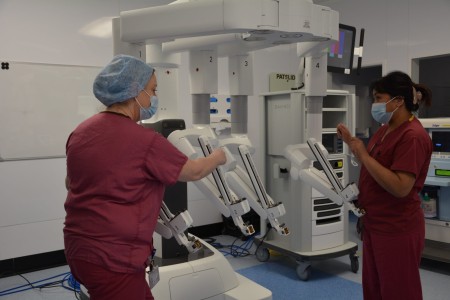 Two women wearing scrubs using a robot.