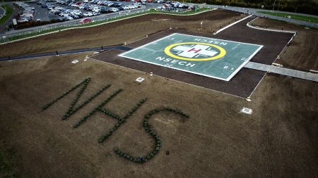A large helipad with NHS written in planting on the bank in front.