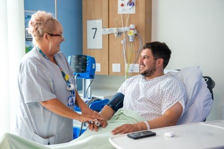 A patient in a bed having his blood pressure and pulse checked.