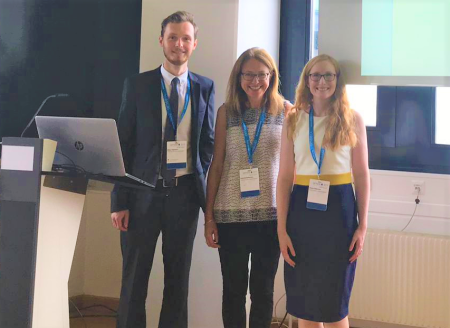 A photograph of three people standing next to a podium.